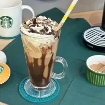 Foto da receita de Frapê de Chocolate. Obseva-se um copo grande decorado com calda de chocolate e chantilly e, ao lado esquerdo, cápsulas de Starbucks.