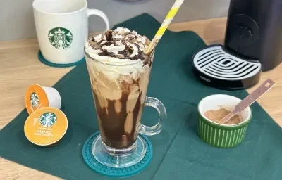 Foto da receita de Frapê de Chocolate. Obseva-se um copo grande decorado com calda de chocolate e chantilly e, ao lado esquerdo, cápsulas de Starbucks.