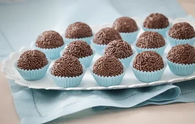 Foto de um prato branco que está em cima de um pano azul com vários brigadeiros dentro de forminhas azuis