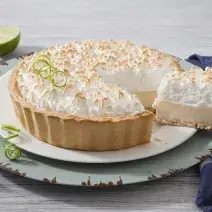 Foto de uma torta de limão em cima de um prato branco e com uma fatia generosa sendo retirada