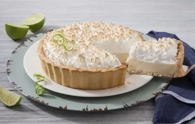 Foto de uma torta de limão em cima de um prato branco e com uma fatia generosa sendo retirada