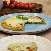 Fotografia em tons de marrom com um prato azul ao centro. Em cima do prato existe uma pizza com massa de Aveia coberta com queijo muçarela e orégano.