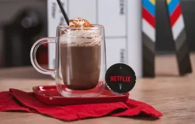 Foto em tons de vermelho e preto da receita de cappuccino netflix servida em um copo largo sobre uma base de porcelana vermelha e um pano vermelho em cima de uma mesa de madeira com uma cápsula de cappuccino netflix ao lado Foto em tons de vermelho e preto da receita de cappuccino netflix servida em um copo largo sobre uma base de porcelana vermelha e um pano vermelho em cima de uma mesa de madeira com uma cápsula de cappuccino netflix ao lado