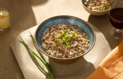 Foto em tons de marrom da receita de risoto de filé mignon e gorgonzola servida em um bowl de cerâmica azul sore um pano bege com ramos de alho poró ao lado Foto em tons de marrom da receita de risoto de filé mignon e gorgonzola servida em um bowl de cerâmica azul sore um pano bege com ramos de alho poró ao lado