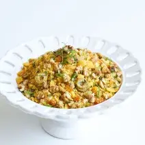 em um prato branco redondo contém a farofa com azeitonas verdes, nozes, damasco