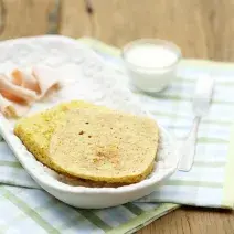 em um recipiente branco contém duas fatias de pão, abaixo dois panos nas cores verde e branco e ao lado uma xícara de leite e um garfo.