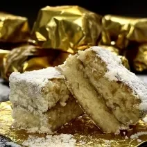 Foto da Receita de Bolo Gelado de 3 leites. Observa-se um bolo cortado ao meio envolto no Leite Ninho em Pó e sobre uma embalagem dourada. Atrás, bolos gelados enroladinhos.