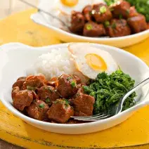 fotografia vista de frente, contém dois recipiente branco e redondo e ambos contém: arroz, couve, pedaços de carne e ovo com um garfo para servir