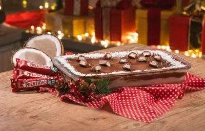 Foto da receita de Pavê de Prestígio. Observa-se o pavê em um recipiente refratário decorado com Prestígios cortados em cima. Atrás, presentes e luzes de Natal decoram a foto. Foto da receita de Pavê de Prestígio. Observa-se o pavê em um recipiente refratário decorado com Prestígios cortados em cima. Atrás, presentes e luzes de Natal decoram a foto.