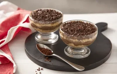 Foto da receita de Bolo de Brigadeiro de Café no Potinho. Observa-se dois potinhos transparentes intercalando uma camada de bolo branco e uma camada de brigadeiro de café. No topo, granulados para decorar. Foto da receita de Bolo de Brigadeiro de Café no Potinho. Observa-se dois potinhos transparentes intercalando uma camada de bolo branco e uma camada de brigadeiro de café. No topo, granulados para decorar.