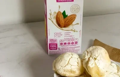 Foto da receita de pão de queijo vegano servida em diversas porções em um prato de porcelana branca sobre uma tábua de madeira com uma embalagem de nature's heart bebida de amêndoa ao fundo