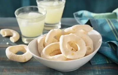 Foto da receita de Biscoito Globo. Observa-se uma tigela com os biscoitos dentro e atrás dois copos de limonada para compor a decoração da foto