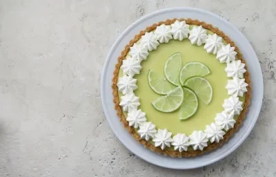 Foto de uma torta limão em cima de um prato branco e com fatias de limão decorando o centro da torta. Foto de uma torta limão em cima de um prato branco e com fatias de limão decorando o centro da torta.