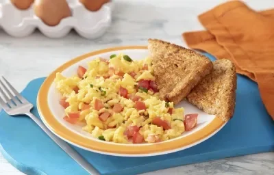 Foto da receita de ovos mexidos cremosos servida em um prato de porcelana branco e laranja junto com duas fatias de pão integral