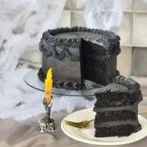 Foto da receita de Bolo de Veludo Preto. Observa-se um bolo alto preto decorado de preto, com uma decoração de Dia das Bruxas.