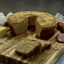 Foto da receita de Pão de Calabresa. Observa-se um pão inteiro no formato de uma forma com furo no meio. Queijo parmesão, linguiça calabresa e ovos decoram a foto