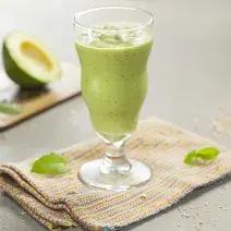 fotografia em tons de cinza e verde de uma bancada cinza vista de frente, contém um pano bege e por cima um copo transparente com a vitamina