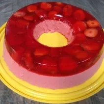 Foto em tons de vermelho da receita de super gelatina de morango servida sobre uma base circular amarela