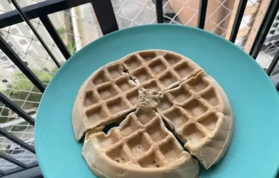 Imagem da receita de Waffle Proteico, em um prato azul, atrás um fundo com a imagem de uma varanda