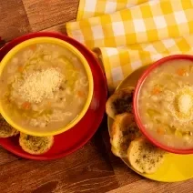 Fotografia mostra duas cumbucas com sopa de carne com legumes e queijo povilhado sobre um prato. Ao lado, torradas temperadas.