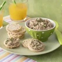 Foto da receita de Pate de Sardinha. Observa-se uma cumbuca verde clara com o patê dentro e, ao lado, biscoitos de arroz servidos com a receita.