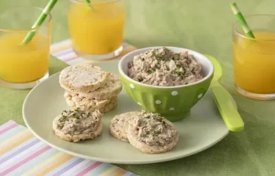 Foto da receita de Pate de Sardinha. Observa-se uma cumbuca verde clara com o patê dentro e, ao lado, biscoitos de arroz servidos com a receita.