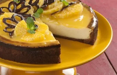 fotografia em tons de roxo, branco e amarelo de uma bancada roxa vista de cima. Contém um suporte para servir sobremesa cor amarelo com uma torta e fatias de laranja por cima. fotografia em tons de roxo, branco e amarelo de uma bancada roxa vista de cima. Contém um suporte para servir sobremesa cor amarelo com uma torta e fatias de laranja por cima.