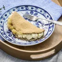 fotografia em tons de marrom, branco e azul tirada de uma tábua de madeira marrom, com um pano azul e por cima um prato redondo azul e branco com a tapioca.
