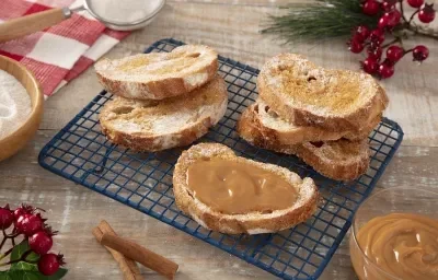 Foto da receita de Rabanada de Doce de Leite feita na Air Fryer. Observa-se 6 rabanadas sobrepostas sobre uma grade azul marinho, sendo que a da frente está com cobertura extra de doce de leite.