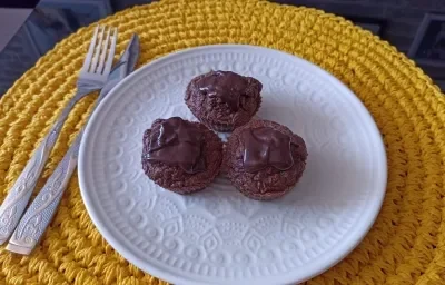 Imagem da receita de Muffin de cacau com coco e cobertura de chocolate meio amargo, em um prato branco, sobre uma mesa e ao lado os talheres