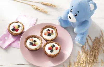 Foto da receita de Cestinha de aveia com iogurte e fruta. Observa-se um pratinho rosa bebê com três cestinhas e uma outra ao lado esquerdo, uma cestinha sobre um guardanapo rosa de bolinhas. Foto da receita de Cestinha de aveia com iogurte e fruta. Observa-se um pratinho rosa bebê com três cestinhas e uma outra ao lado esquerdo, uma cestinha sobre um guardanapo rosa de bolinhas.