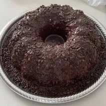 Foto em tons de marrom da receita de bolo cenourolate servida em uma porção grande sobre uma forma descartável branca