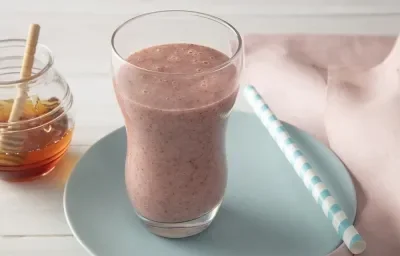 Foto da receita de smoothie iogurte molico com morango e chia servida em um copo largo sobre um pratinho azul com um canudo listrado ao lado junto deum paninho rosa. Ao fundo há um vidro de mel Foto da receita de smoothie iogurte molico com morango e chia servida em um copo largo sobre um pratinho azul com um canudo listrado ao lado junto deum paninho rosa. Ao fundo há um vidro de mel