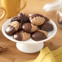 Foto da receita de Biscoitinho de Cappuccino. Observa-se uma boleira branca com 8 biscoitinhos em cima, banhados pela metade com chocolate.