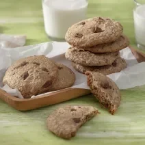 Foto da receita de Cookie Vegano. Observa-se 7 cookies dispostos em uma tábua de madeira, sendo que um está cortado ao meio.