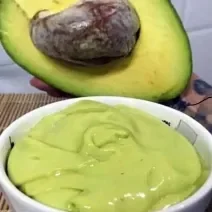 Foto da receita de Mousse de Abacate. Observa-se um potinho branco com a mousse cremosa dentro e um abacate pela metade atrás ilustrando.