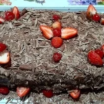 Foto em tons de marrom da receita de bolo de chocolate com morangos servida inteira e decorada com morangos e cerejas em cima