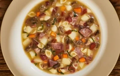 Foto bem aproximada de um prato branco fundo no qual está a receita pronta de sopão de carne com legumes e linguiça