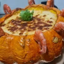 Foto da receita de camarão na moranga servida em uma moranga grande com camarões ao redor sobre uma base de torta de alumínio