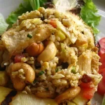 Fotografia de arroz com castanhas, com tomate e pepino decorando ao lado, dentro de um prato branco.