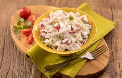 Foto da receita de saladinha de macarrão no copinho servida em um copo largo amarelo sobre um paninho verde com um garfo prateado ao lado, há também, em cima da tábua de madeira, tomates cerejas cortados ao meio Foto da receita de saladinha de macarrão no copinho servida em um copo largo amarelo sobre um paninho verde com um garfo prateado ao lado, há também, em cima da tábua de madeira, tomates cerejas cortados ao meio