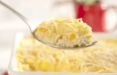 Foto de uma colher em primeiro plano, suspensa e com fricassê. No segundo plano da foto há uma forma branca com mais fricassê