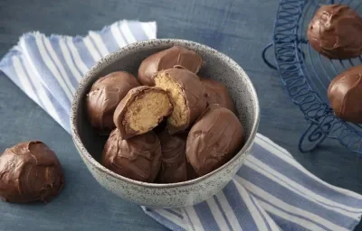 Foto da receita de Bombom de Farinha Láctea NESTLÉ Aveia. Observa-se um recipiente de cerâmica com 7 bombons dentro, sendo que o de cima está cortado ao meio e é possível ver o interior do bombom