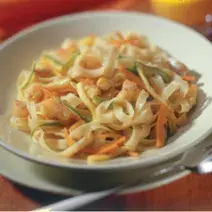Fotografia em tons de marrom e branco de uma bancada marrom vista de cima, um prato branco com macarrão e cenoura e ao lado um garfo para servir.