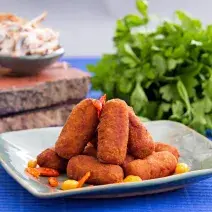 Foto da receita de croquete de carne, servidos em um prato acinzentado, sobre uma bancada azul com um maço de salsinha ao fundo