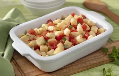 Foto da receita de Nhoque sem Glúten. Observa-se um refratário retangular branco com o nhoque dentro ao molho de tomate, decorado com folhas de manjericão. Foto da receita de Nhoque sem Glúten. Observa-se um refratário retangular branco com o nhoque dentro ao molho de tomate, decorado com folhas de manjericão.