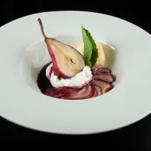 Fotografia de uma sobremesa gelada de pera cozida no vinho com um pouco de creme de leite por cima, juntamente de uma bola de sorvete de creme e uma folha de hortelã. A sobremesa está dentro de um prato branco com o meio fundo.