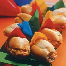 fotografia tirada de vários mini sanduíches enrolados em panos nas cores vermelho, amarelo verde e azul.