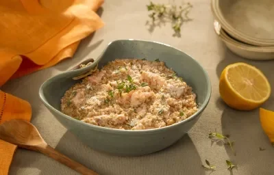 Foto da receita de risoto de salmão com grana padano servida em um bowl de cerâmica azul sobre uma mesa cinza com um limão siciliano cortado ao meio ao lado