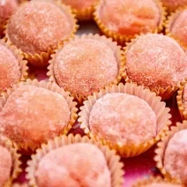 Fotografia de vários docinhos de cor rosa em pequenas forminhas. Cada um dos docinhos está polvilhado com açúcar